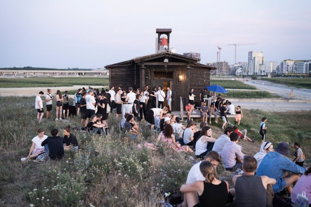 Menschenmenge vor Horlzhütte mit Stadt im Hintergrund