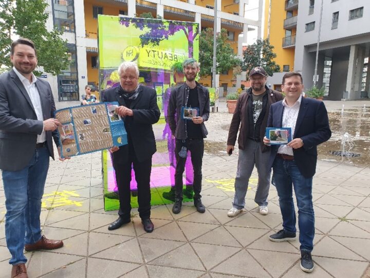 Fünf Männer mit einem Plakat vor eienem durchsichtigen rechteckigen Kubus