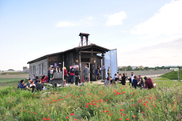 Holzhaus mit Leuten auf Wiese