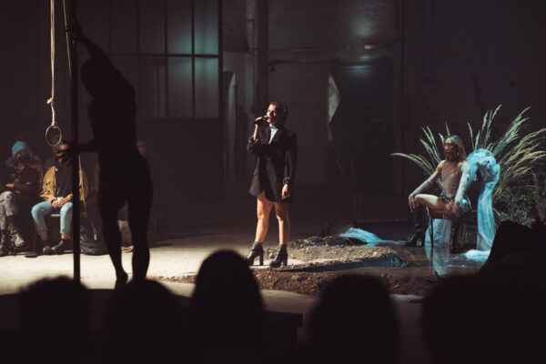 Eine Person auf einem Thron mit Ähren, eine andere spricht ins Microphon, Publikum im Hintergrund