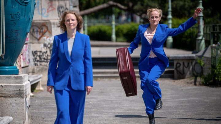 2 Frauen in blauem Hosenanzug, eine geht, die andere springt