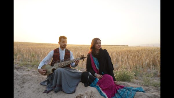 Zwei Musiker:innen in traditioneller Kleidung sitzend im Kornfeld