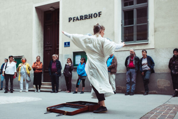 Performerin neben offenem Koffer auf straße mit Publikum