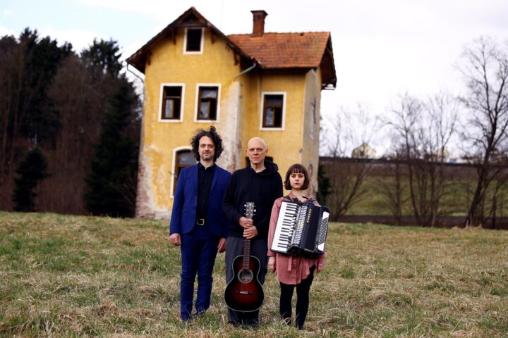 3 Personen vor altem Haus mit Musikinstrumenten