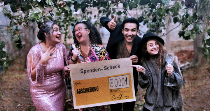 4 Personen in festlichen Outfits mit freudigem Gesichtsausdruck halten einen Spenden-Scheck auf dem steht "für Abschiebung EUR 0001"