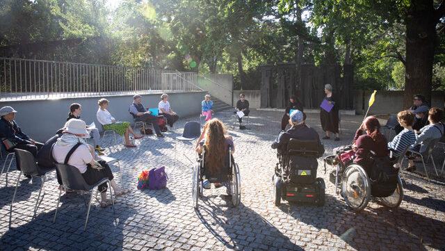 Personen auf einem Platz im Freien im Sesselkreis mit und ohne Rollstuhl
