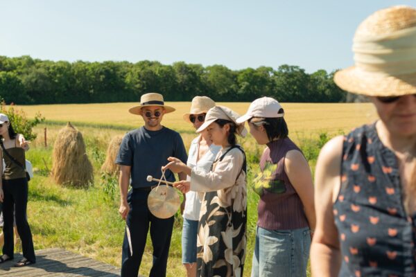 Four people stand in a field addressing an audience. One of them is holding a gong.