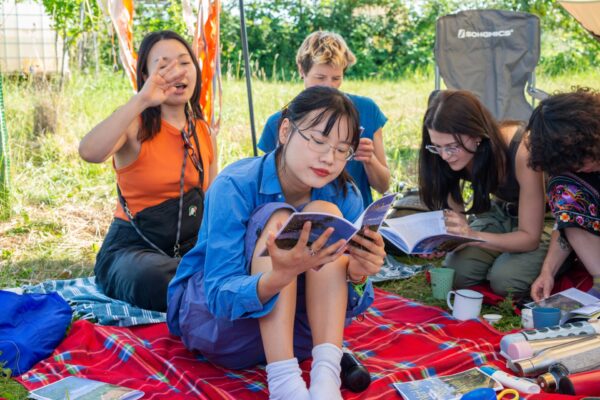 A girl sits in the foreground reading a booklet with three other girls sitting behind her.