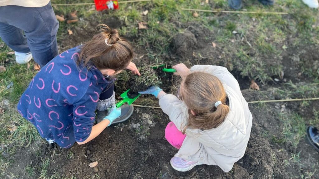 Zwei Kinder hocken in einem Garten und schaufeln Erde.